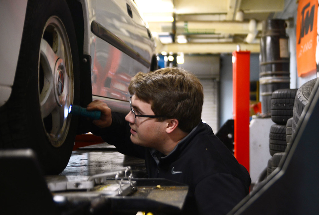 Senior Alex Masson uses a flashlight to check the tires of a car that was raised up by the car lift. Photo by Grace Goldman