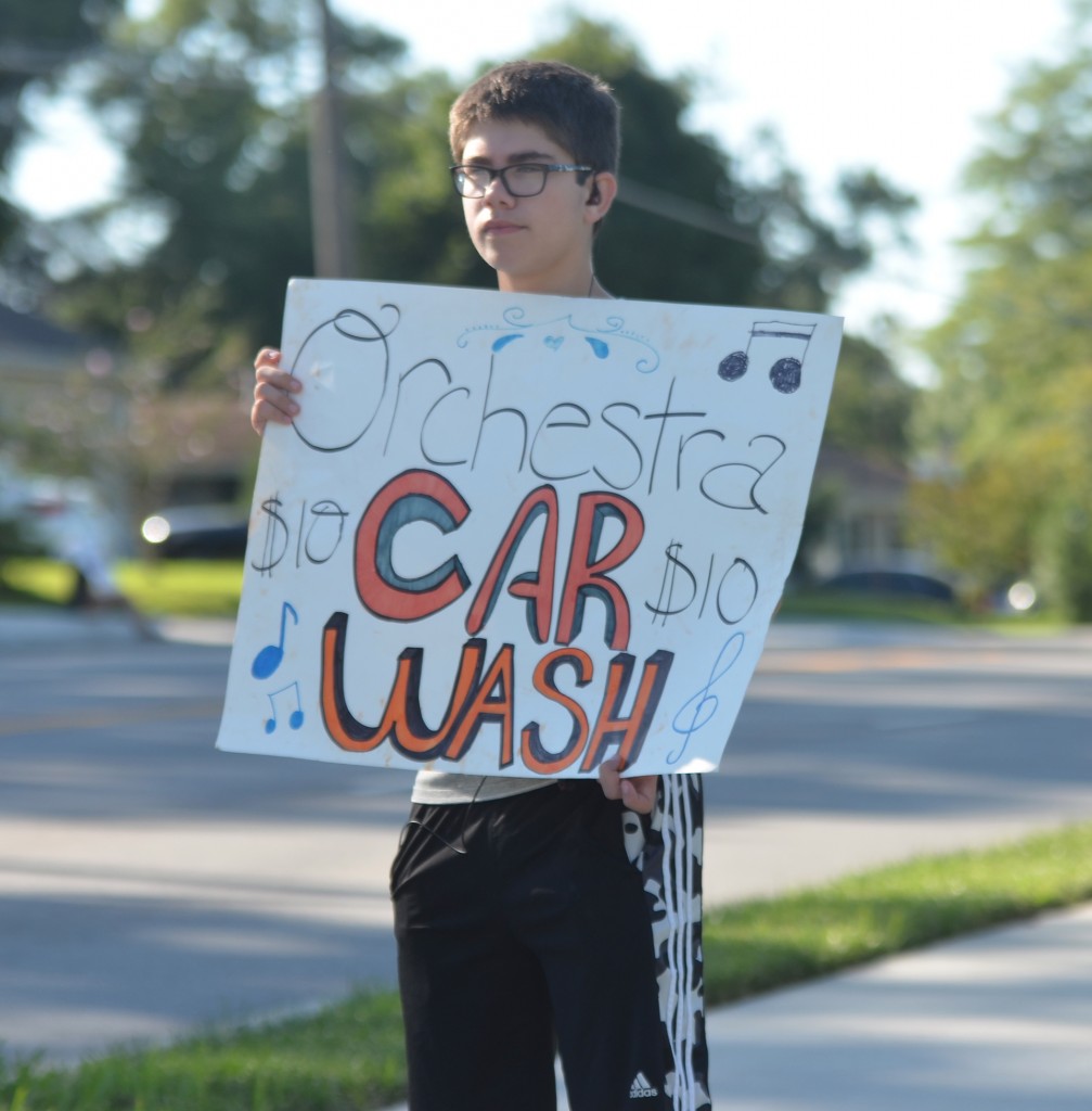 Freshman Charlie Pacunski holds up a sign on Mission road to drum up business for the car wash. Photo by Taylor Keal.