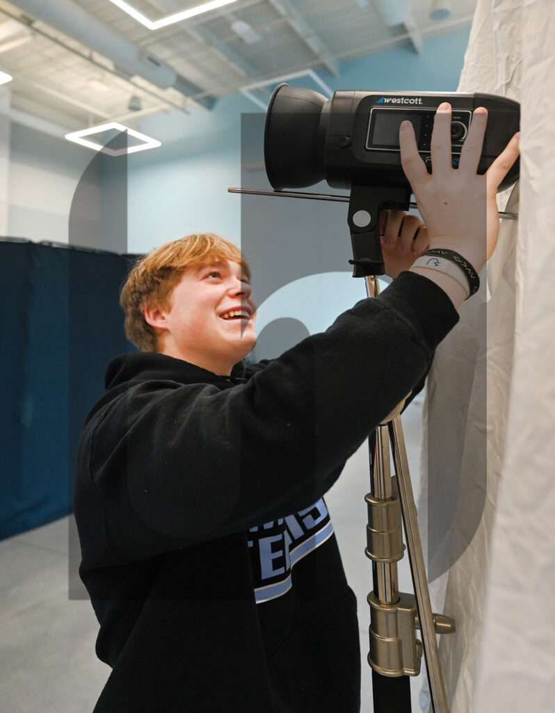 Junior and assistant photo editor Tyler Russell sets up a light for a backdrop. “I put the bedskirt around the umbrella which helps diffuse the light,” Russell said. Photo by Addie Clark