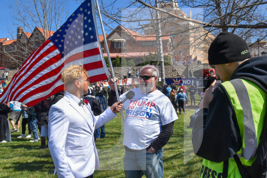 A protester holds an American flag while getting interviewed for a YouTube video. Photo by Avra Welling